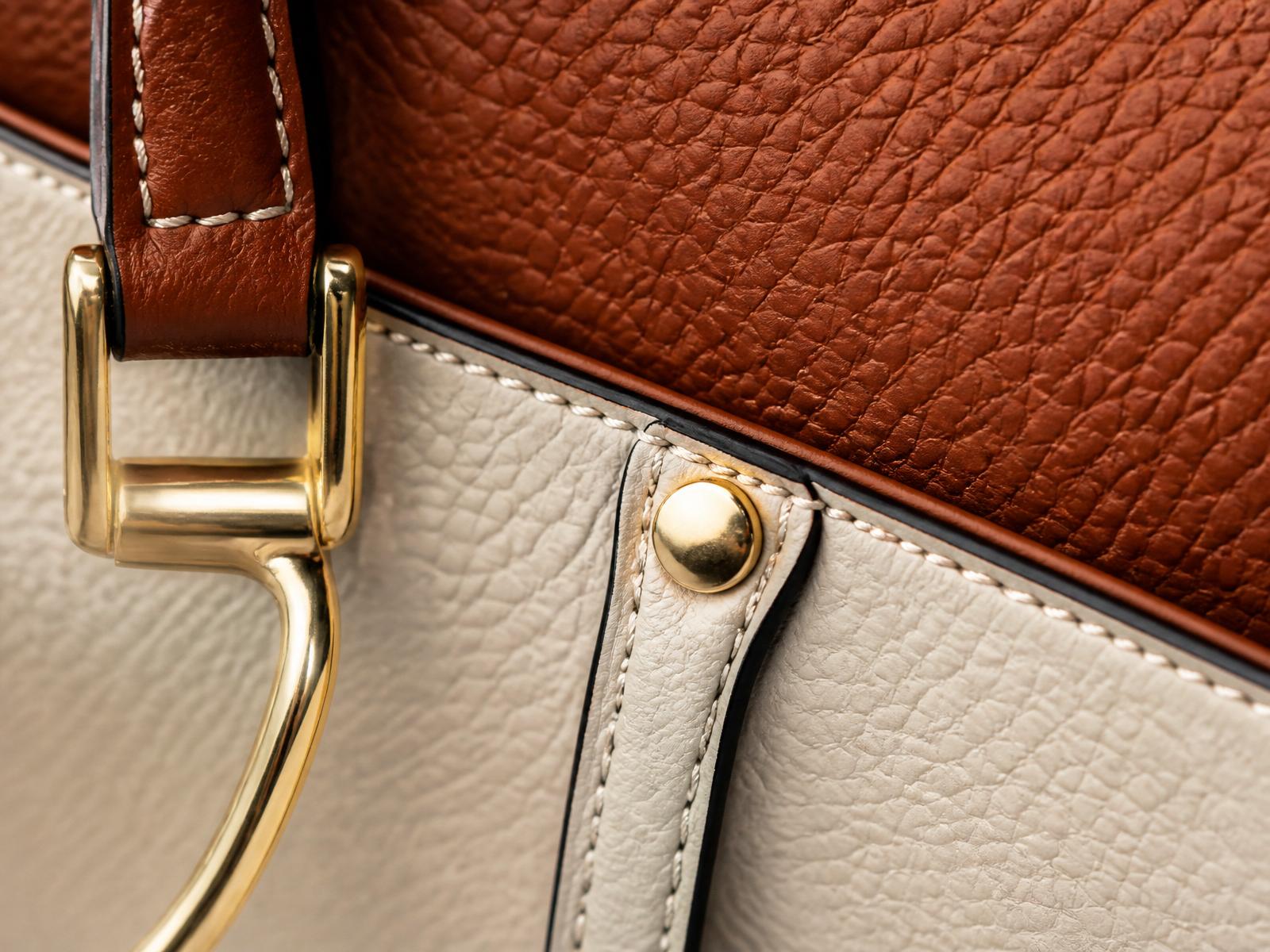 Macro detail of two-tone cognac and cream pebbled leather with polished brass hardware